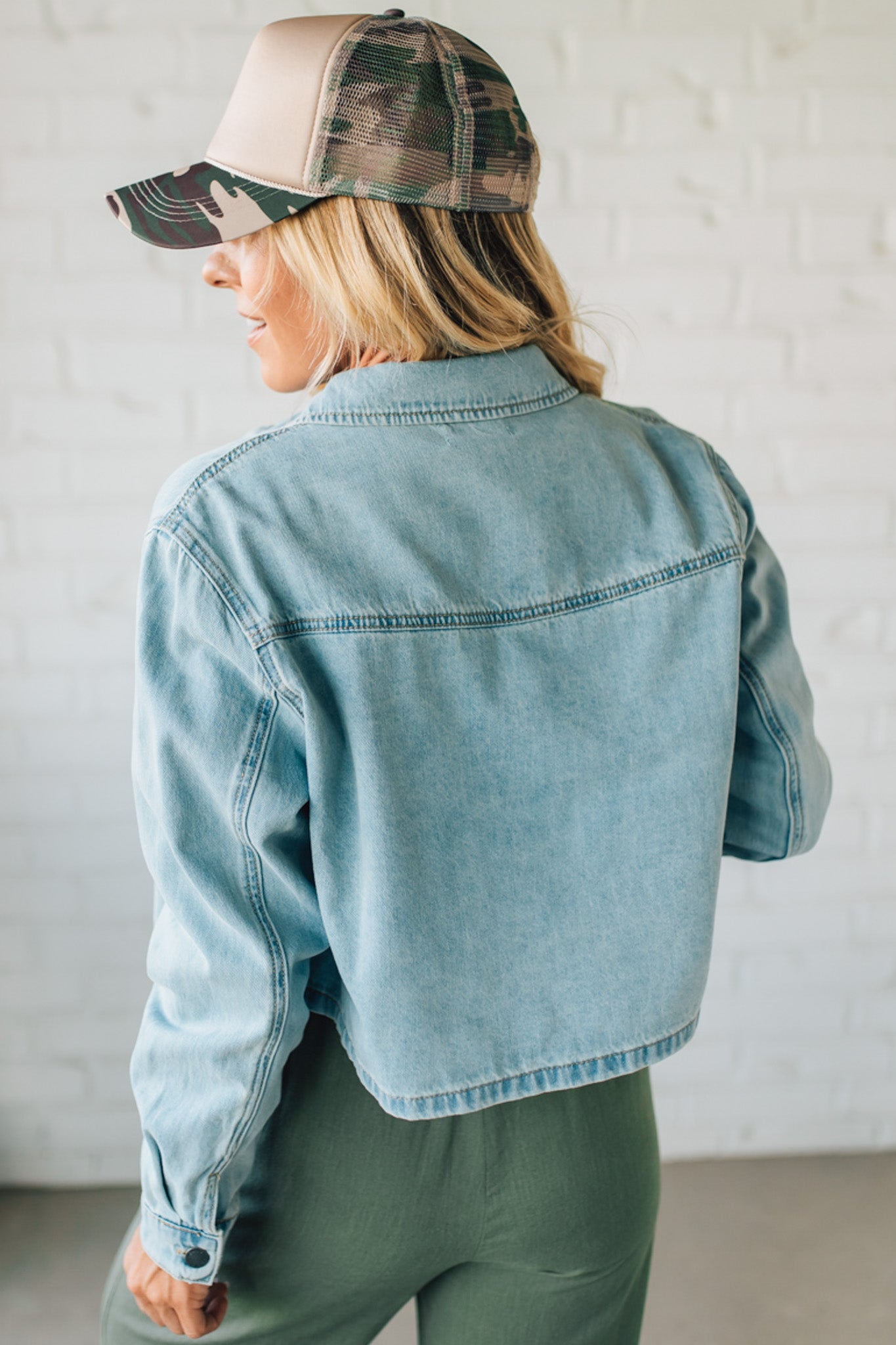Person wearing a light blue denim jacket and green cap with a neutral background