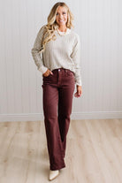 BLONDE WOMAN IN A BRIGHTLY LIT STUDIO WEARING A PAIR OF BROWN JEANS, CREAM CHUNKY BEADED NECKLACE AND A WAFFLED GRID SWEATER IN CREAM AND OLIVE GREEN.