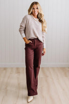 BLONDE WOMAN IN A BRIGHTLY LIT STUDIO WEARING A PAIR OF BROWN JEANS, CREAM CHUNKY BEADED NECKLACE AND A WAFFLED GRID SWEATER IN CREAM AND BROWN.