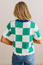 A woman viewed from the back wearing a short-sleeve knit top with a green and white checkerboard pattern and a blue ribbed collar, paired with blue jeans.