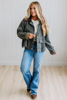 Blonde woman wearing a leopard print barn jacket with brown corduroy collar and gingham plant lining. Standing on a light wood floor with panel backdrop.