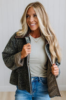 Blonde woman wearing a leopard print barn jacket with brown corduroy collar and gingham plant lining. Standing on a light wood floor with panel backdrop.