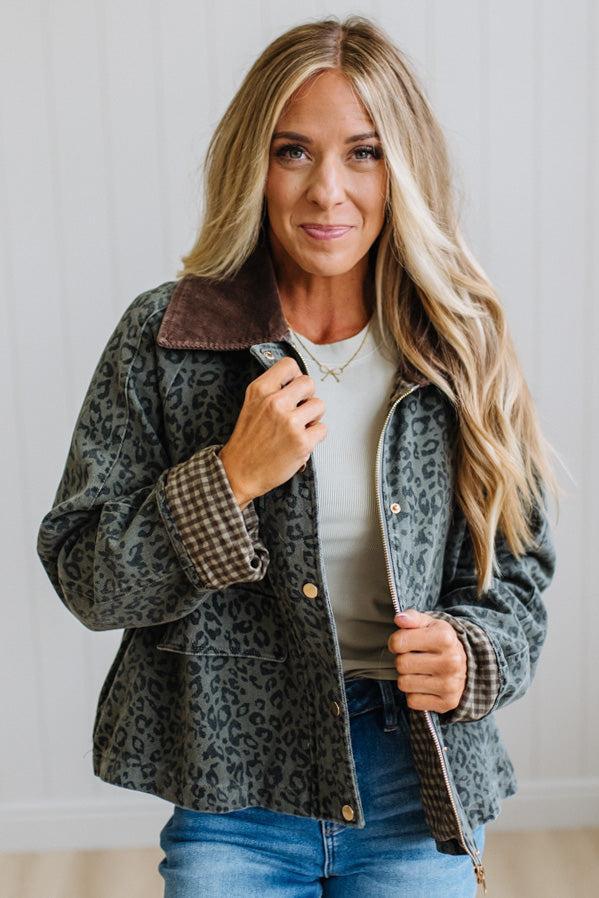 Blonde woman wearing a leopard print barn jacket with brown corduroy collar and gingham plant lining. Standing on a light wood floor with panel backdrop.