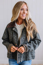 Blonde woman wearing a leopard print barn jacket with brown corduroy collar and gingham plant lining. Standing on a light wood floor with panel backdrop.