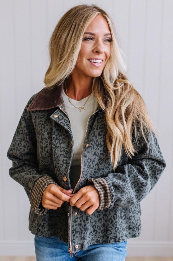 Blonde woman wearing a leopard print barn jacket with brown corduroy collar and gingham plant lining. Standing on a light wood floor with panel backdrop.