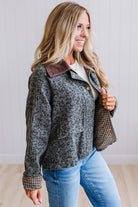 Blonde woman wearing a leopard print barn jacket with brown corduroy collar and gingham plant lining. Standing on a light wood floor with panel backdrop.