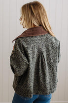 A woman shown from the back wearing a cropped leopard-print jacket with a brown suede-like collar, paired with blue jeans, against a white paneled wall.