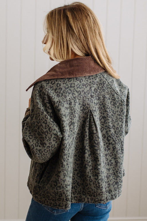 A woman shown from the back wearing a cropped leopard-print jacket with a brown suede-like collar, paired with blue jeans, against a white paneled wall.