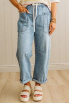 Person wearing light blue jeans and white sandals on a wooden floor.