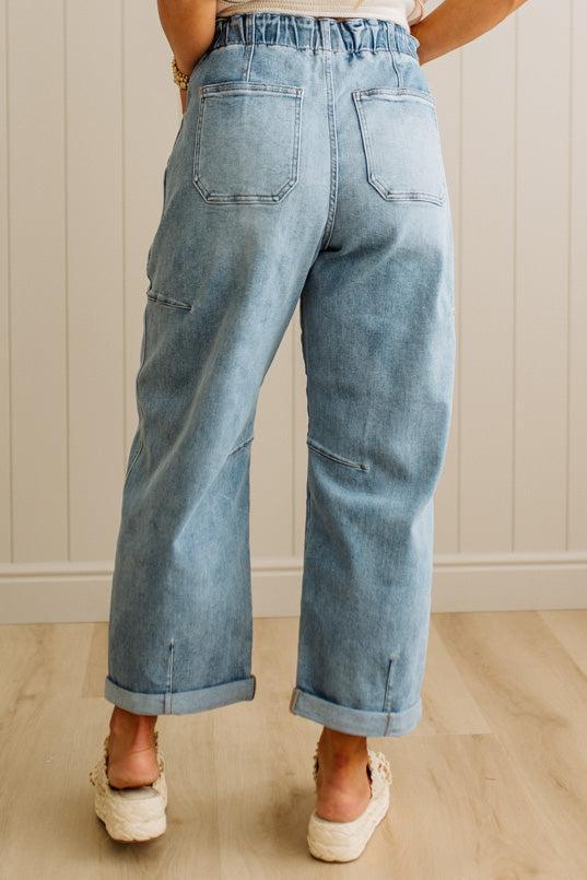 Person wearing light blue jeans standing on a wooden floor with a neutral wall background