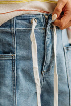 Close-up of a person adjusting the waistband of blue jeans.