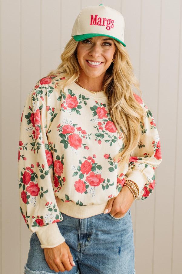 Woman wearing a floral sweatshirt and cap with 'Margs' text against a neutral background
