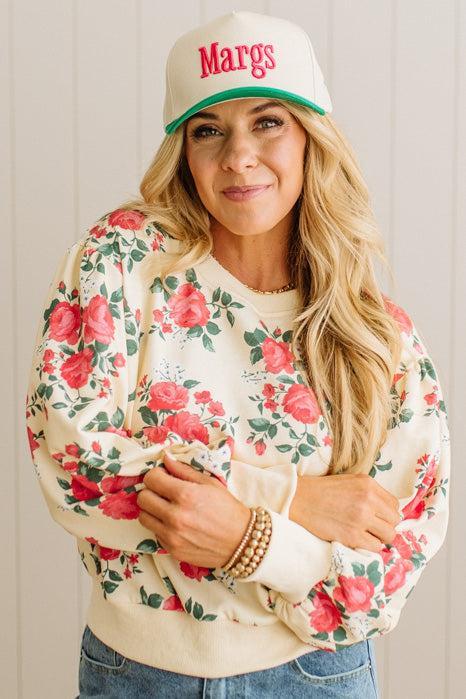 Woman wearing a floral sweatshirt and cap with 'Margs' text.