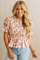 Woman wearing a floral peplum top and light blue jeans against a neutral background