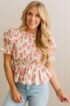 Woman wearing a floral blouse and light blue jeans against a neutral background