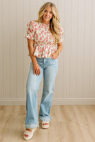 Woman wearing a floral top and light blue jeans standing against a beige wall.