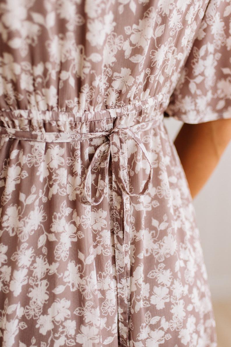 Close-up of a dusty mauve short-sleeve dress with a white floral print and a matching fabric tie belt at the waist.