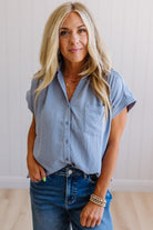 Woman wearing a light blue button-up shirt and jeans against a plain background