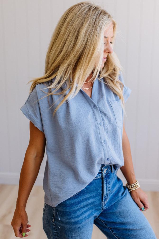 Woman wearing a light blue sleeveless shirt and jeans against a plain background