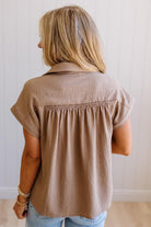 Person wearing a beige short-sleeve shirt against a plain background