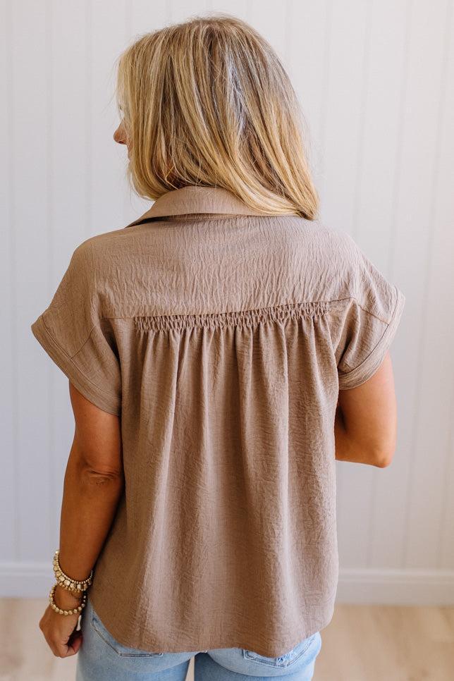 Person wearing a beige short-sleeve shirt against a plain background