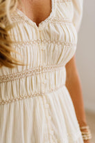 Close-up of a cream-colored bohemian-style dress with delicate embroidery, button details, and a smocked waist, worn by a model.