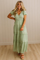 Woman wearing a light green dress standing against a beige wall.