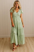 Woman wearing a green dress standing against a beige wall.