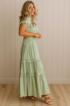 Woman wearing a light green tiered dress standing against a beige paneled wall.