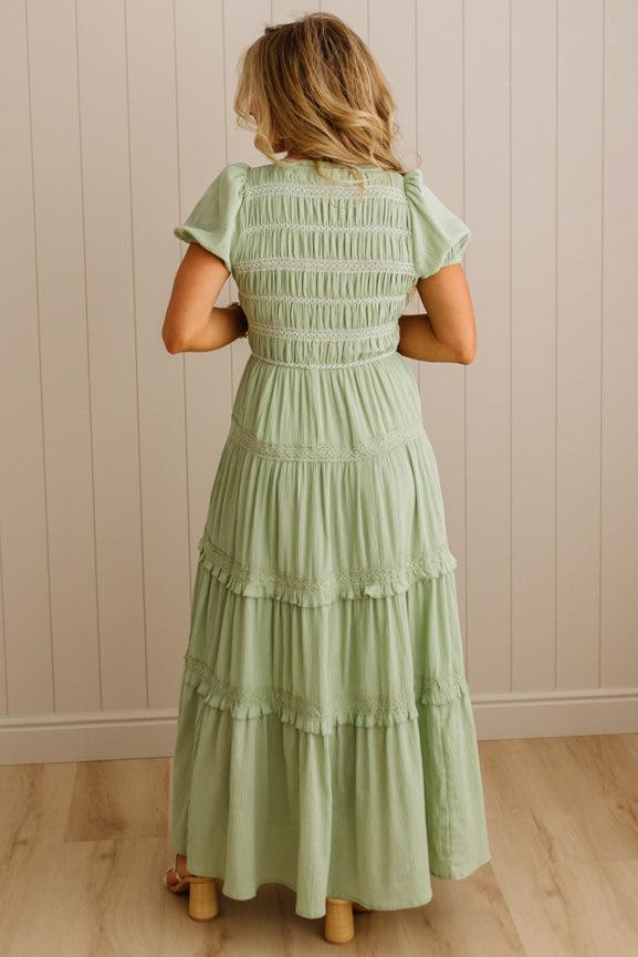 Woman wearing a light green dress with ruffled sleeves and layered skirt against a beige wall.