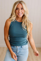 Woman wearing a teal sleeveless top and light blue jeans, standing against a plain background.