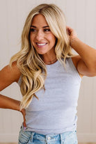 Woman with long blonde hair wearing a gray tank top and blue jeans against a plain background