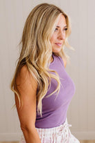 Woman wearing a purple sleeveless top with a neutral background