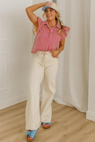 Woman wearing a red and white striped shirt, beige pants, and blue sandals indoors.