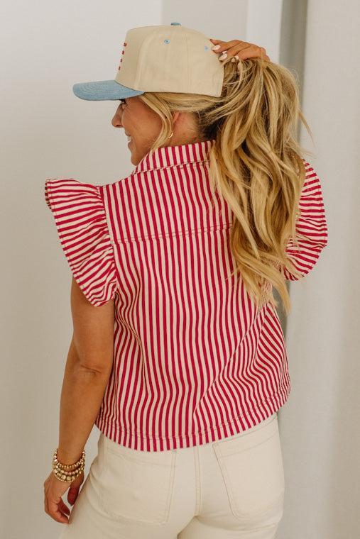Woman wearing a red and white striped shirt with a beige cap, standing against a plain background.