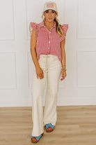 Woman wearing a red and white striped shirt, white pants, and a cap with an American flag design.