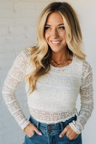 Woman wearing a white lace top and blue jeans against a light background