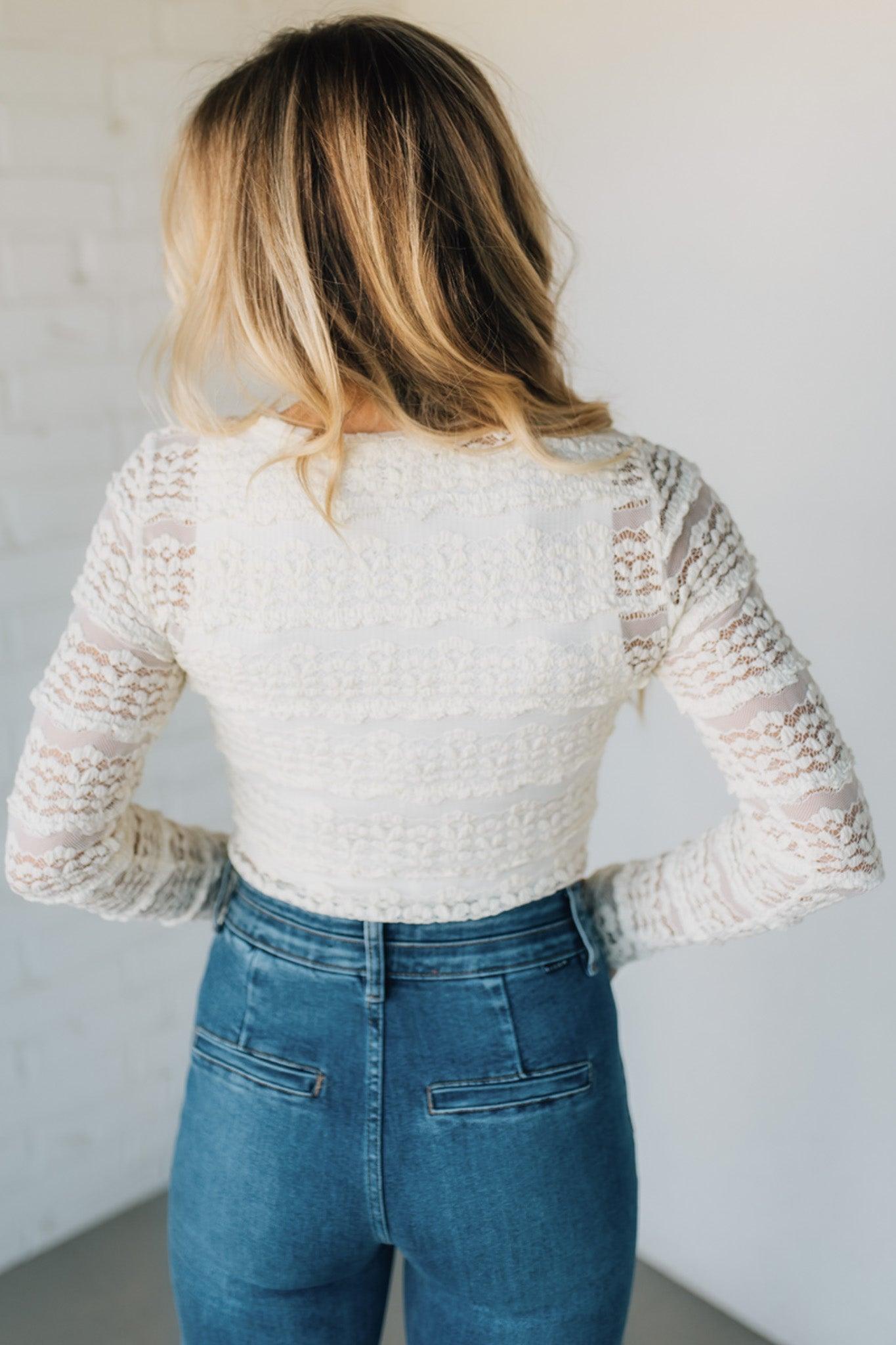 Person wearing a white lace top and blue jeans against a plain background