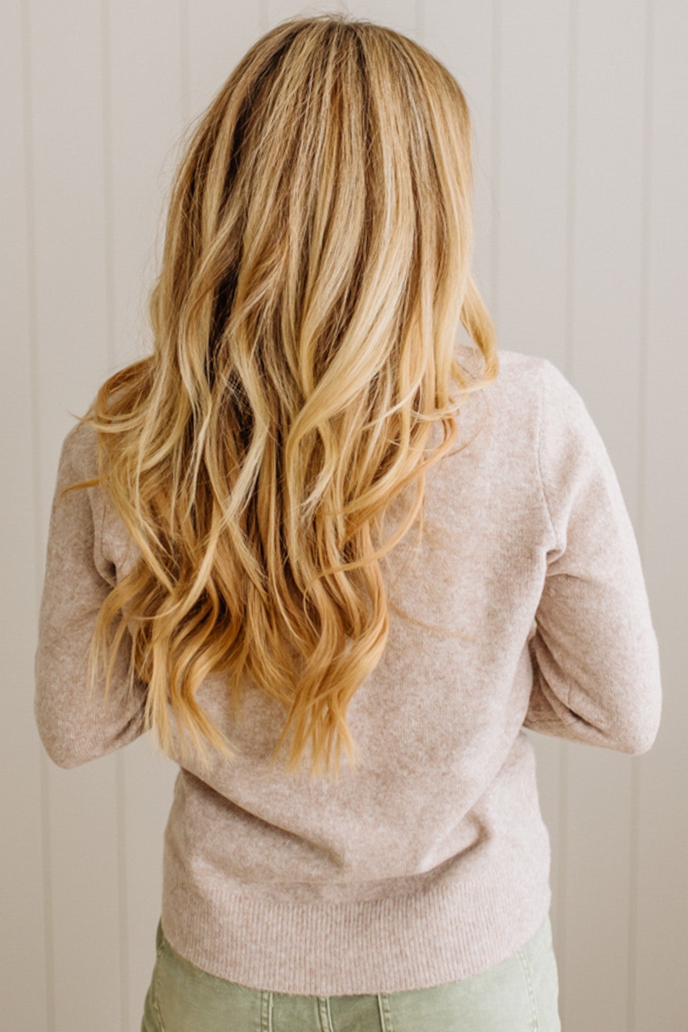 Person with long blonde hair wearing a beige sweater against a neutral background