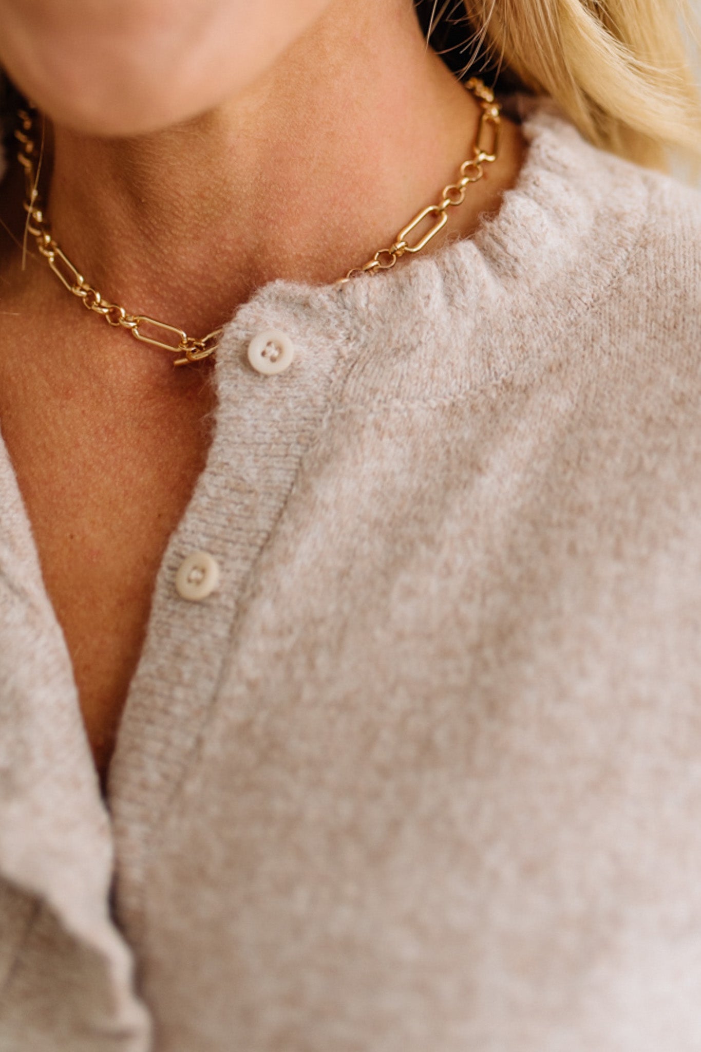 Close-up of a person wearing a gold chain necklace with a neutral-colored cardigan.
