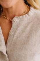Close-up of a person wearing a gold chain necklace with a neutral-colored cardigan.