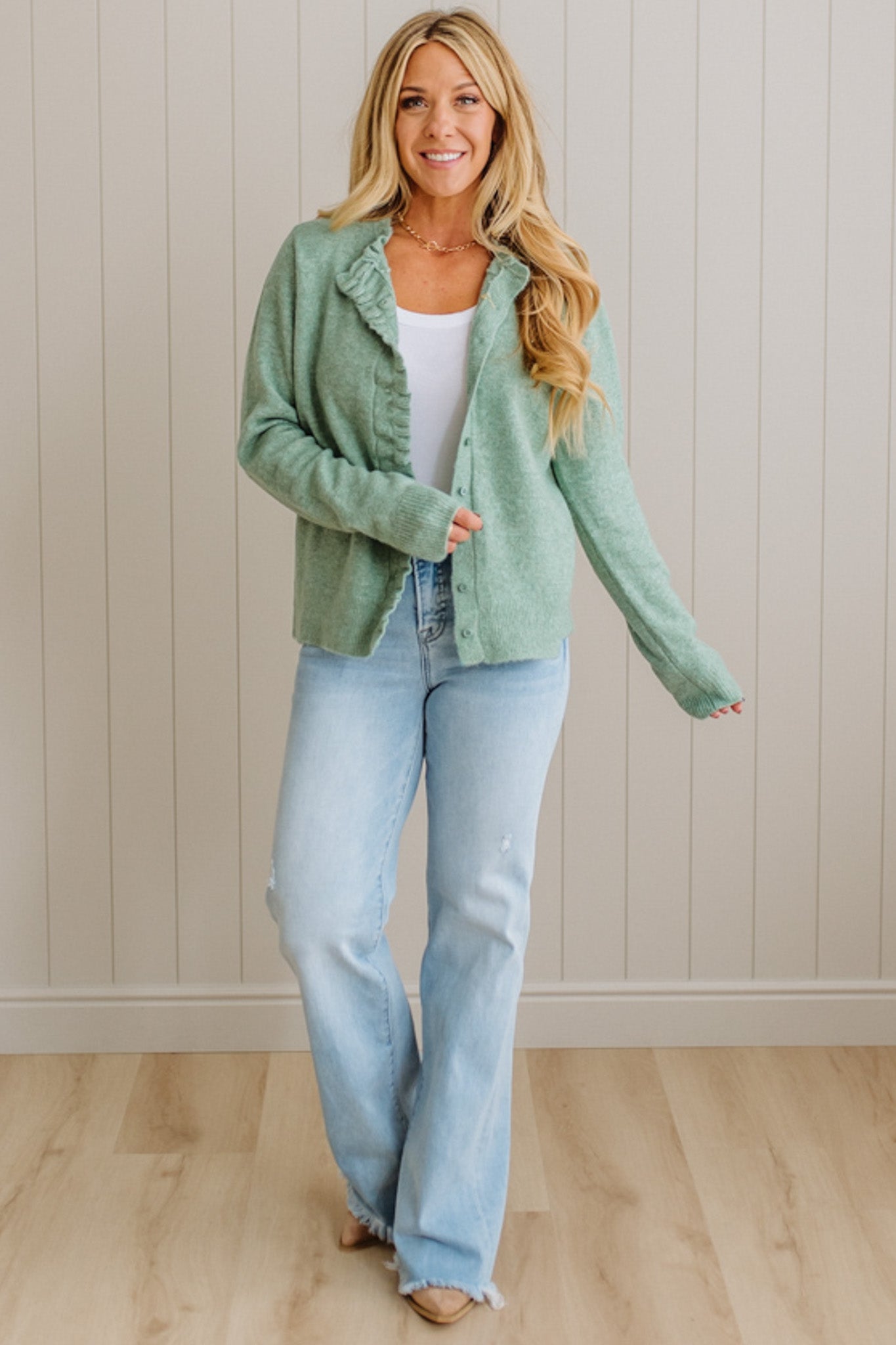 Woman wearing a green jacket and blue jeans against a beige wall.