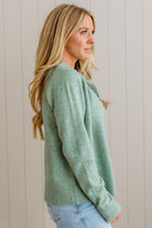 Woman wearing a green sweater against a light wooden panel background