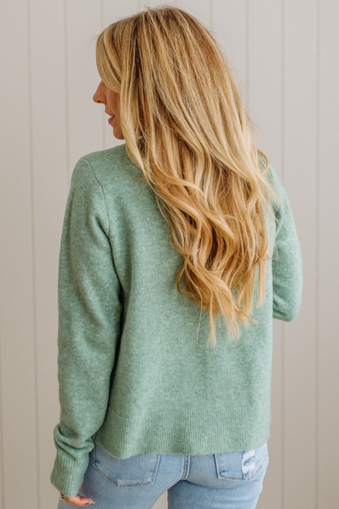 Person wearing a green sweater and blue jeans against a neutral background