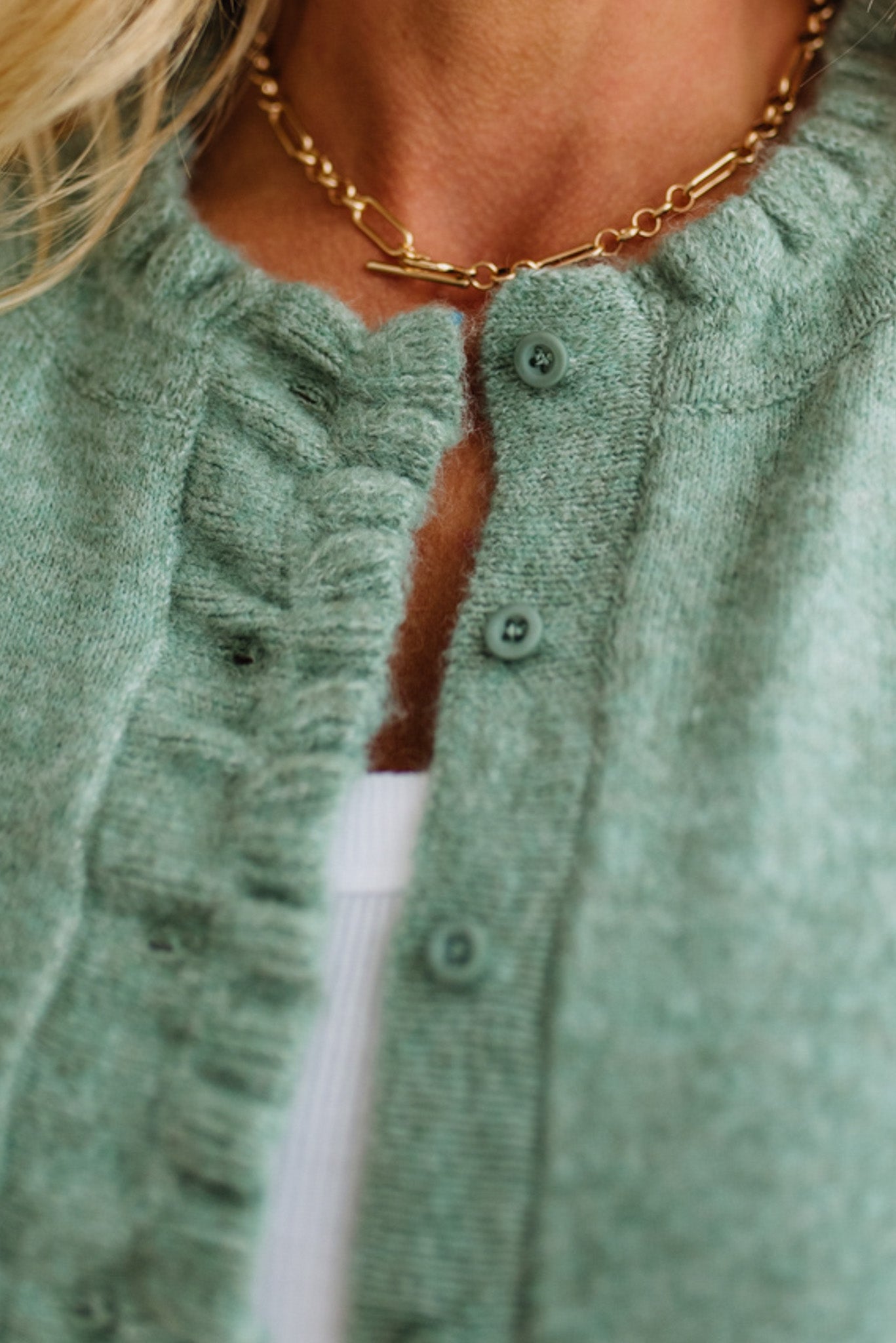 Close-up of a person wearing a green cardigan with a gold chain necklace.
