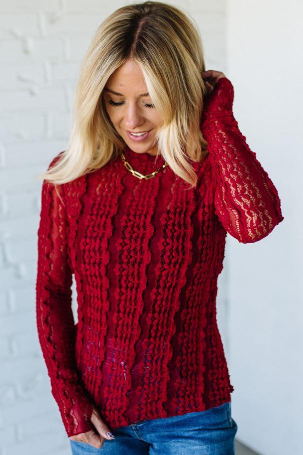 Woman wearing a red mesh lace top against a white background