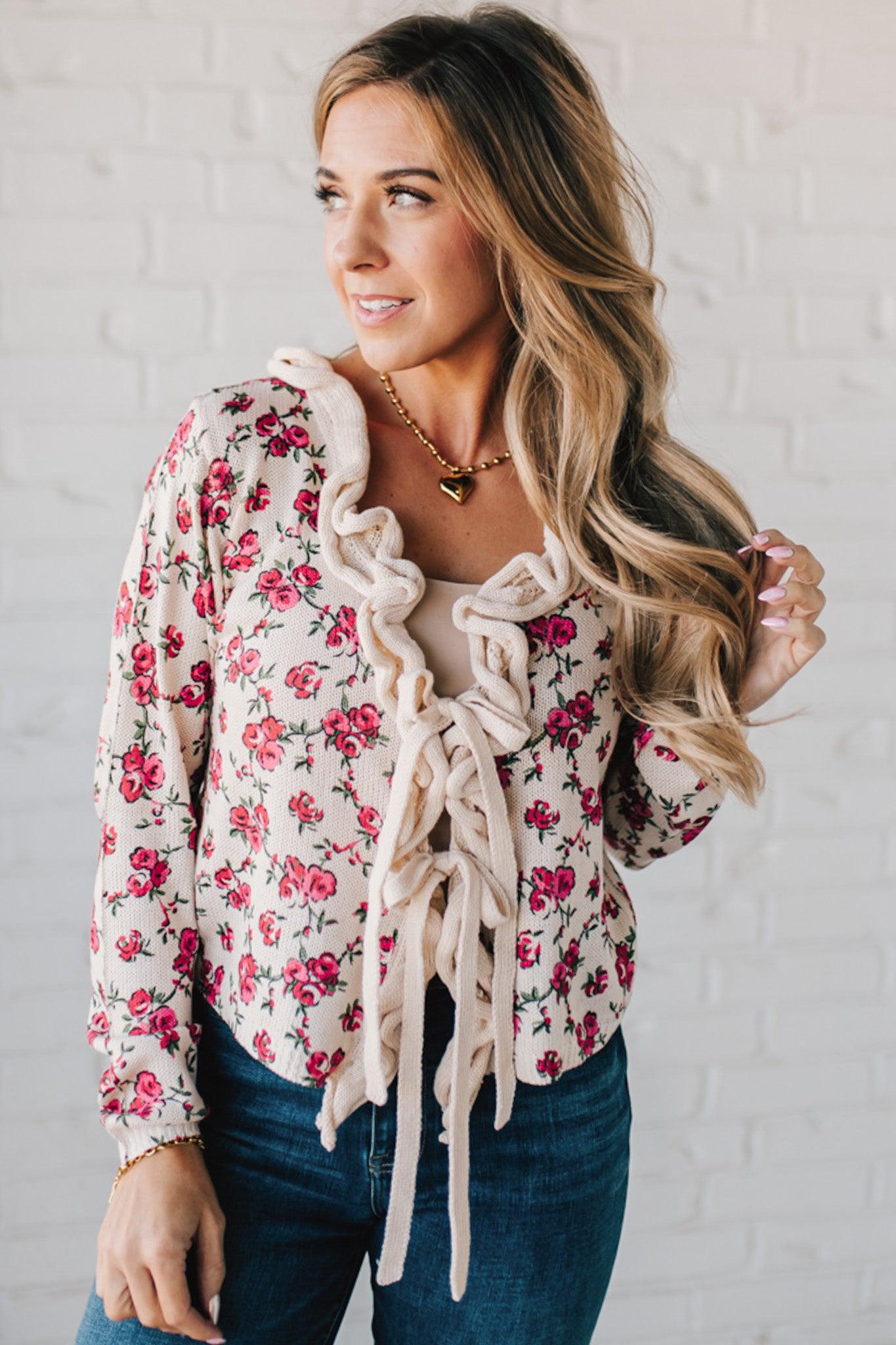 blonde girl modeling a long sleeve cream colored cardigan with a pink floral pattern and ruffle edge detail