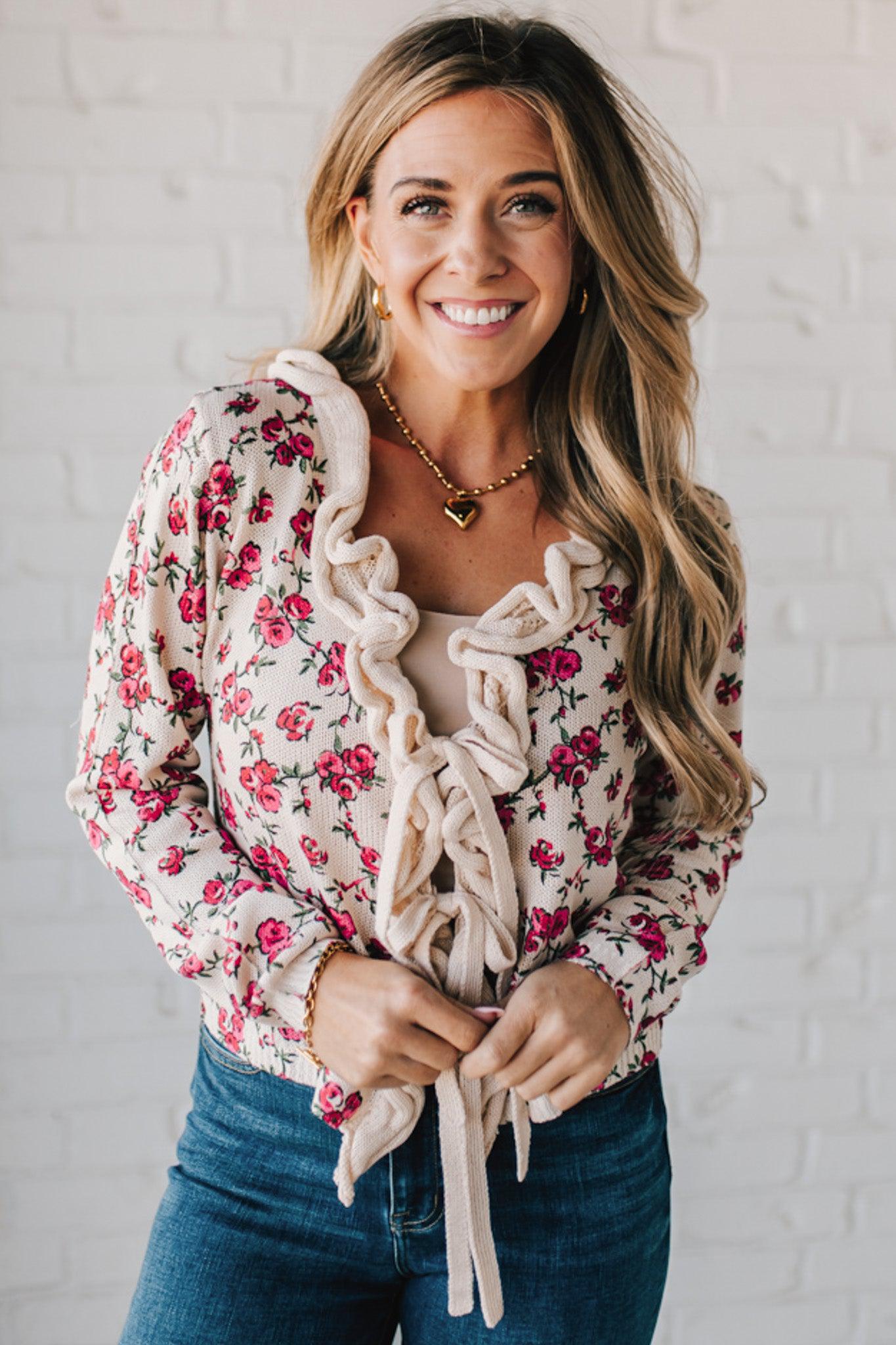 blonde girl modeling a long sleeve cream colored cardigan with a pink floral pattern and ruffle edge detail