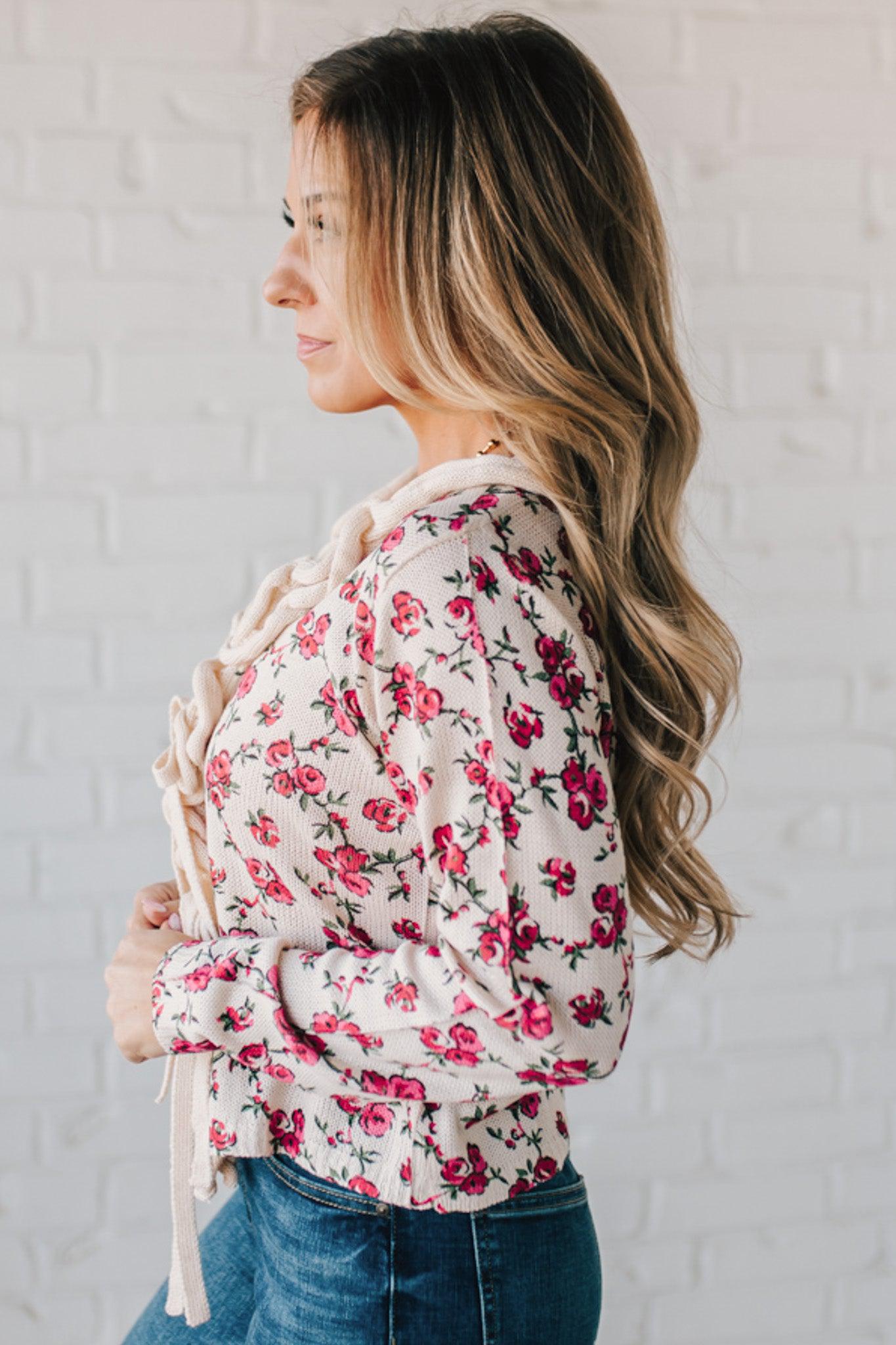 blonde girl modeling a long sleeve cream colored cardigan with a pink floral pattern and ruffle edge detail