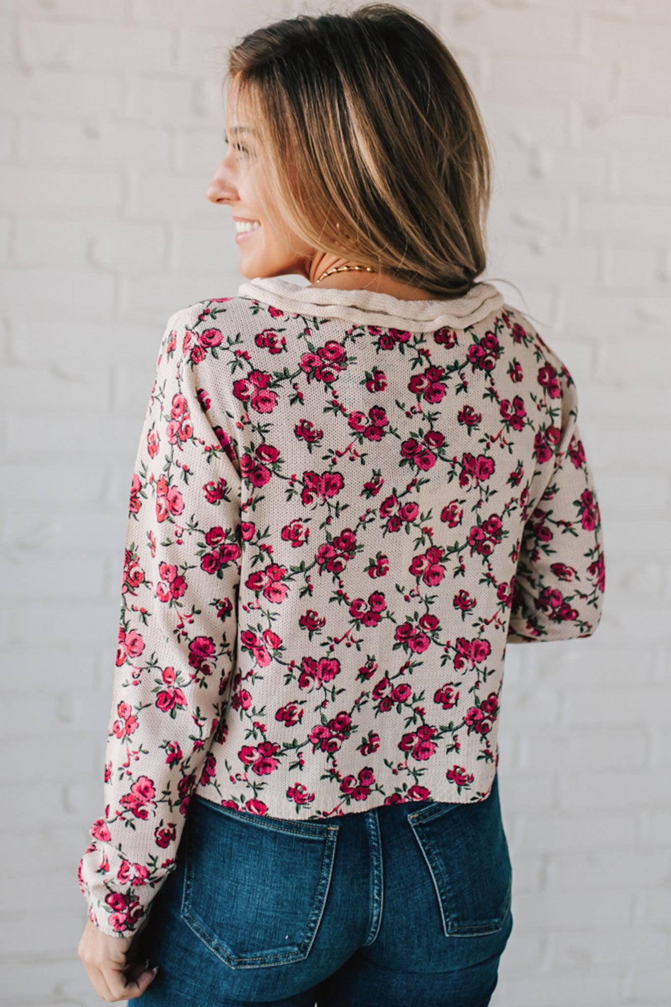 blonde girl modeling a long sleeve cream colored cardigan with a pink floral pattern and ruffle edge detail